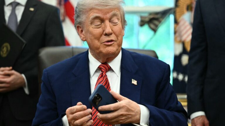 Trump killed the Digital Equity Act, but US was forced to bring part of it back President Trump sitting at his desk in the White House while holding a smartphone in his left hand.
